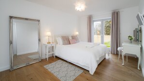 A bedroom with a large mirror, a bed with white bedding, a bedside table with a lamp, and a desk with a mirror. - Taymore Lodge, your home away from home... (Kenmore)