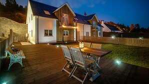 A two-story house with a wooden deck, a dining area with a table and chairs, and a stone wall. - Taymore Lodge, your home away from home... (Kenmore)