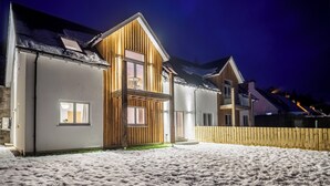 A two-story house with a wooden facade and a balcony, set against a snowy landscape at night. - Taymore Lodge, your home away from home... (Kenmore)