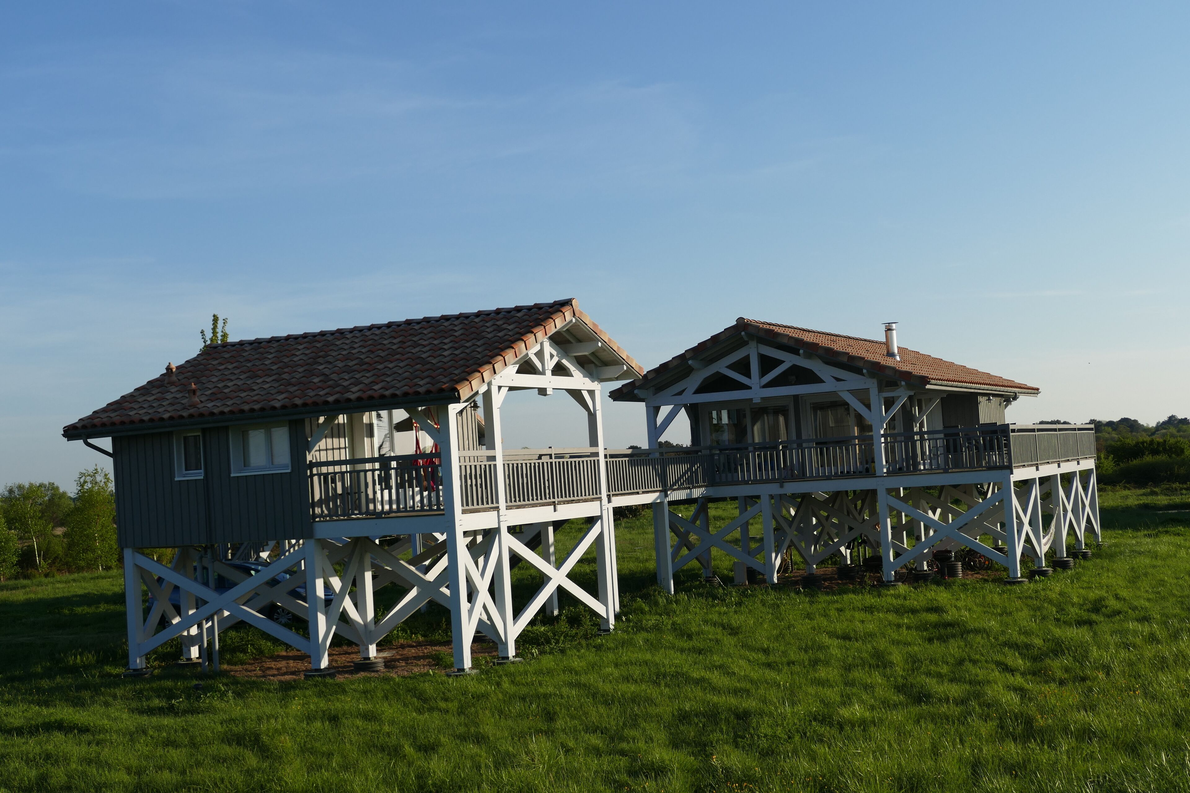Deux cabanes en bois, dotées de balcons et de rampes blanches, sont situées sur un terrain herbeux.