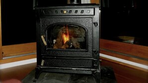 A black wood-burning stove with a glass door, a visible fire inside, and a window to the left. - House / Villa - Talais (Talais)