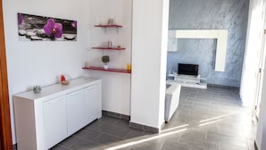 Une cuisine moderne avec des meubles blancs, un plan de travail rouge et une étagère murale agrémentée d’objets décoratifs.