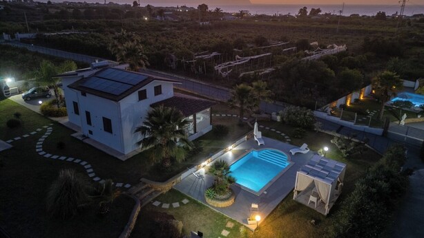 Une maison moderne dotée d’une piscine, de panneaux solaires et offrant une vue sur l’océan au coucher du soleil.