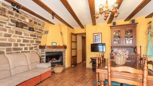 Ein gemütliches Wohnzimmer mit Steinwand, Kamin, einer Couch und einem Esstisch mit Stühlen.
