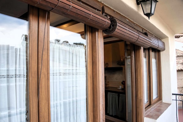 A wooden-framed window with a curtain, a kitchen visible inside, and a balcony with a railing.