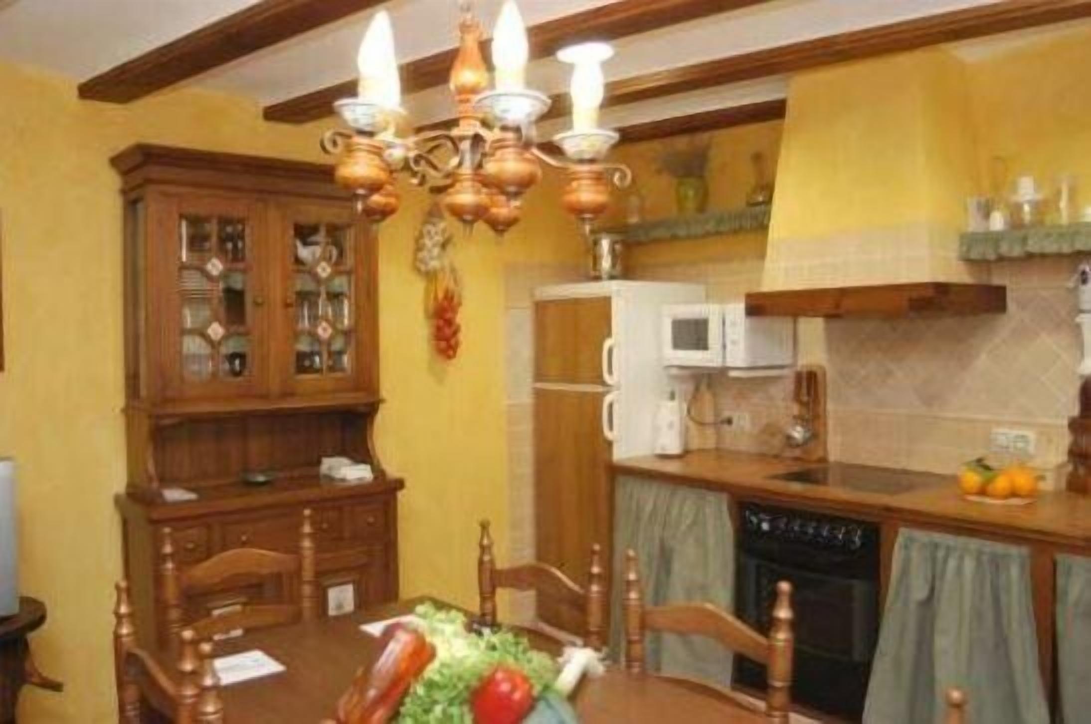A dining area with a wooden table, chairs, a chandelier, and a kitchen with a microwave and oven.
