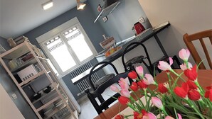Una cucina moderna con zona pranzo, caratterizzata da una finestra con persiane, una macchina da caffè e un vaso di tulipani sul tavolo.