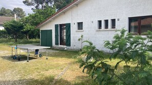 Valkoinen rakennus, jossa on vihreät ikkunaluukut, pöytätennispöytä ja vehreä ympäristö.