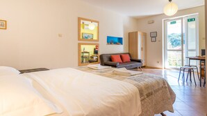 A hotel room with a bed, a sofa, a dining table with chairs, and a large window with an exit sign.