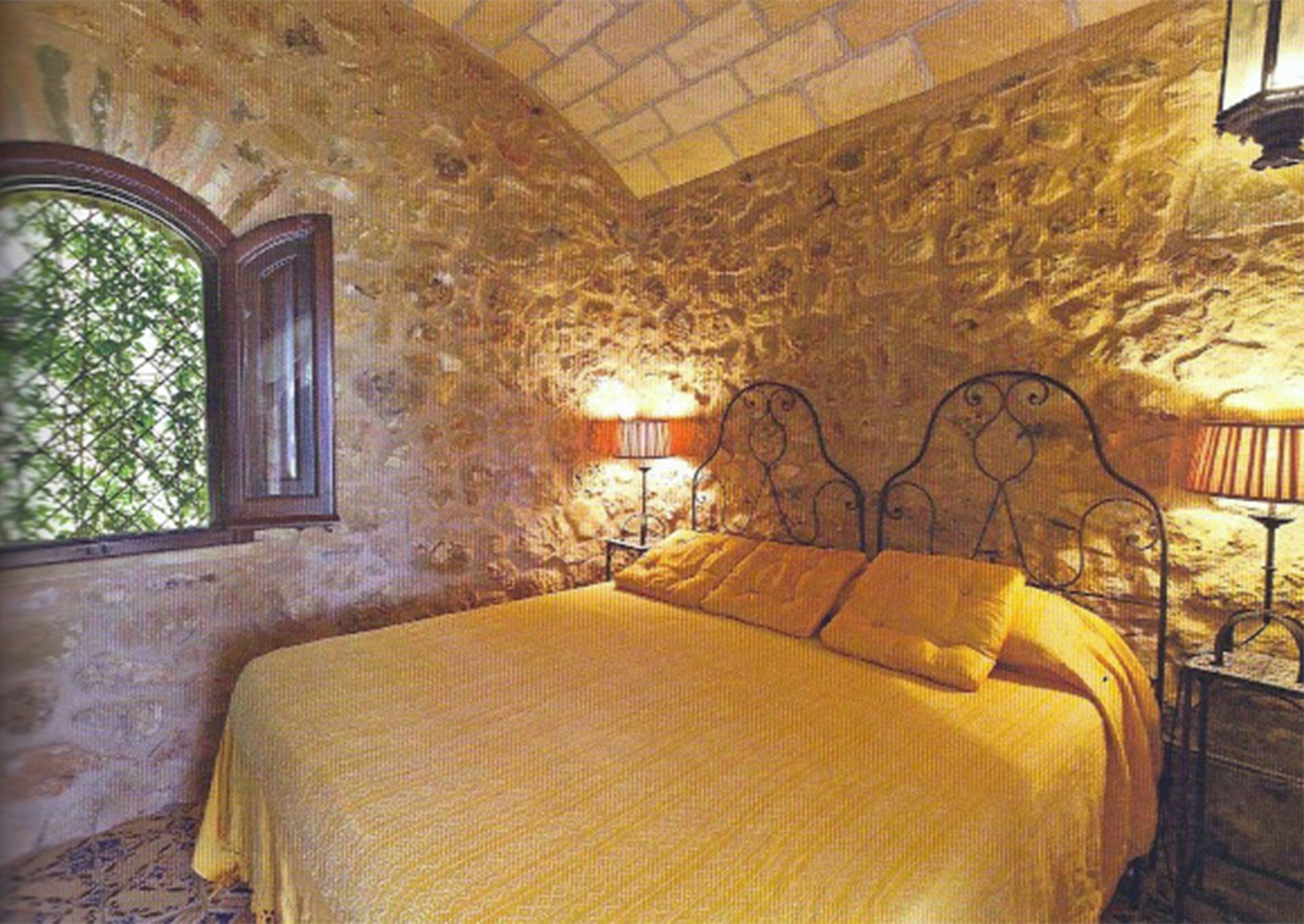 Une chambre aux murs de pierre, avec un lit, une fenêtre et une lampe.