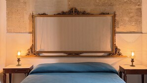 Een slaapkamer met een groot bed, twee nachtkastjes met lampen, een decoratief hoofdeinde en een stenen muur achter het bed.