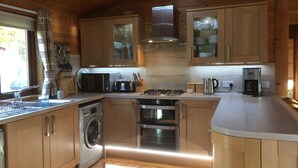 Cocina compacta con armarios de madera, estufa de acero inoxidable, horno integrado, lavadora y cafetera.