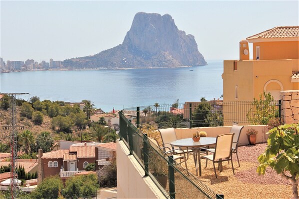 A terrace with a table and chairs overlooking a body of water and a mountain.