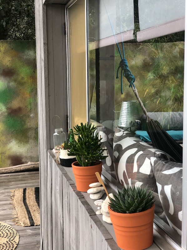A window with a view of a garden, a potted plant, and a hammock.