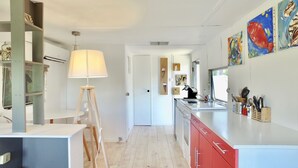 A modern kitchen with a white countertop, red cabinets, and a wooden floor. There is a lamp with a white shade, a sink, and various kitchen utensils. - Zen cabin in the bush (Bonifacio)