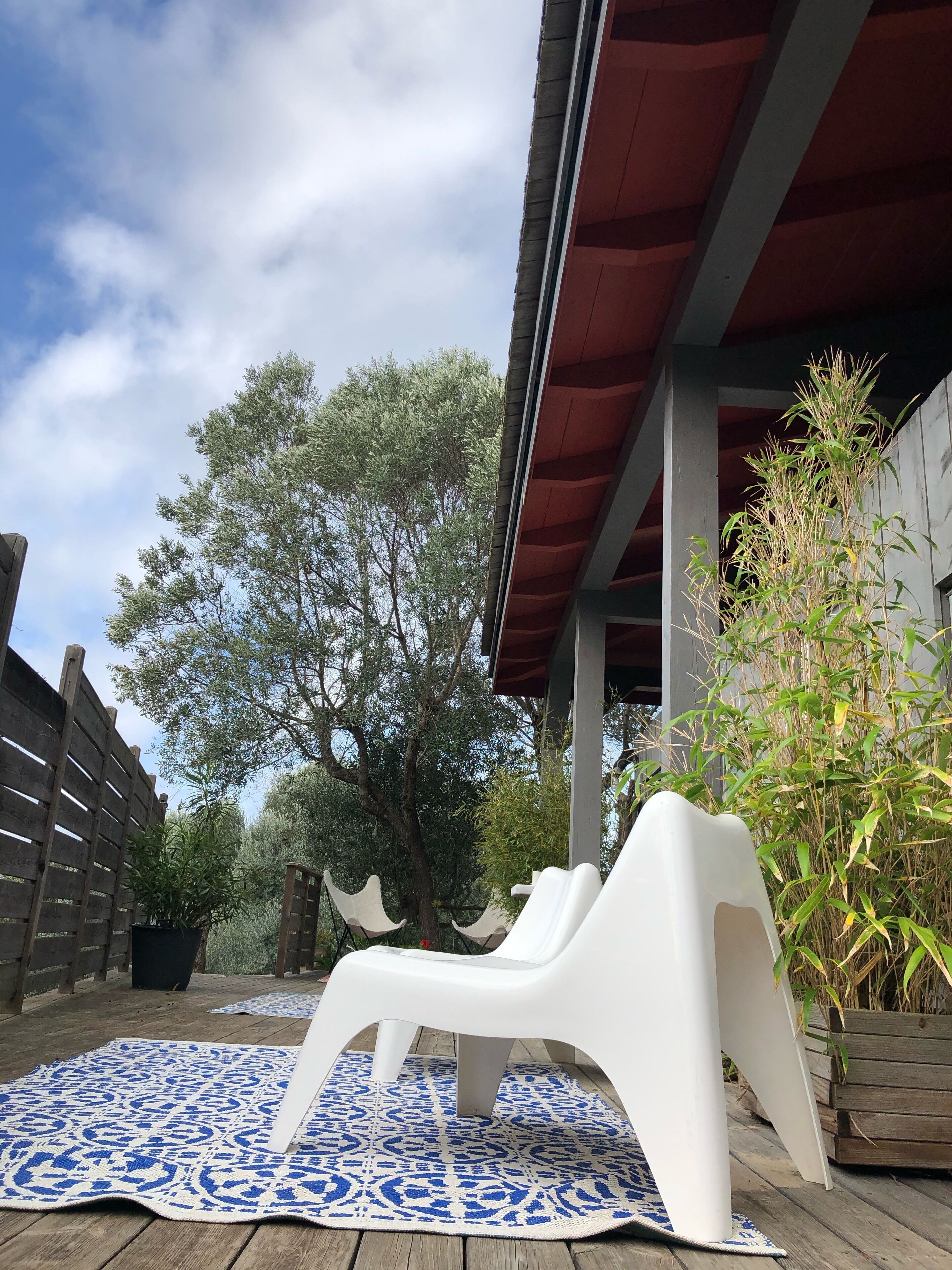 Un espacio al aire libre cubierto con una silla lounge blanca sobre un tapete de diseño azul, una terraza de madera y una cerca de madera.