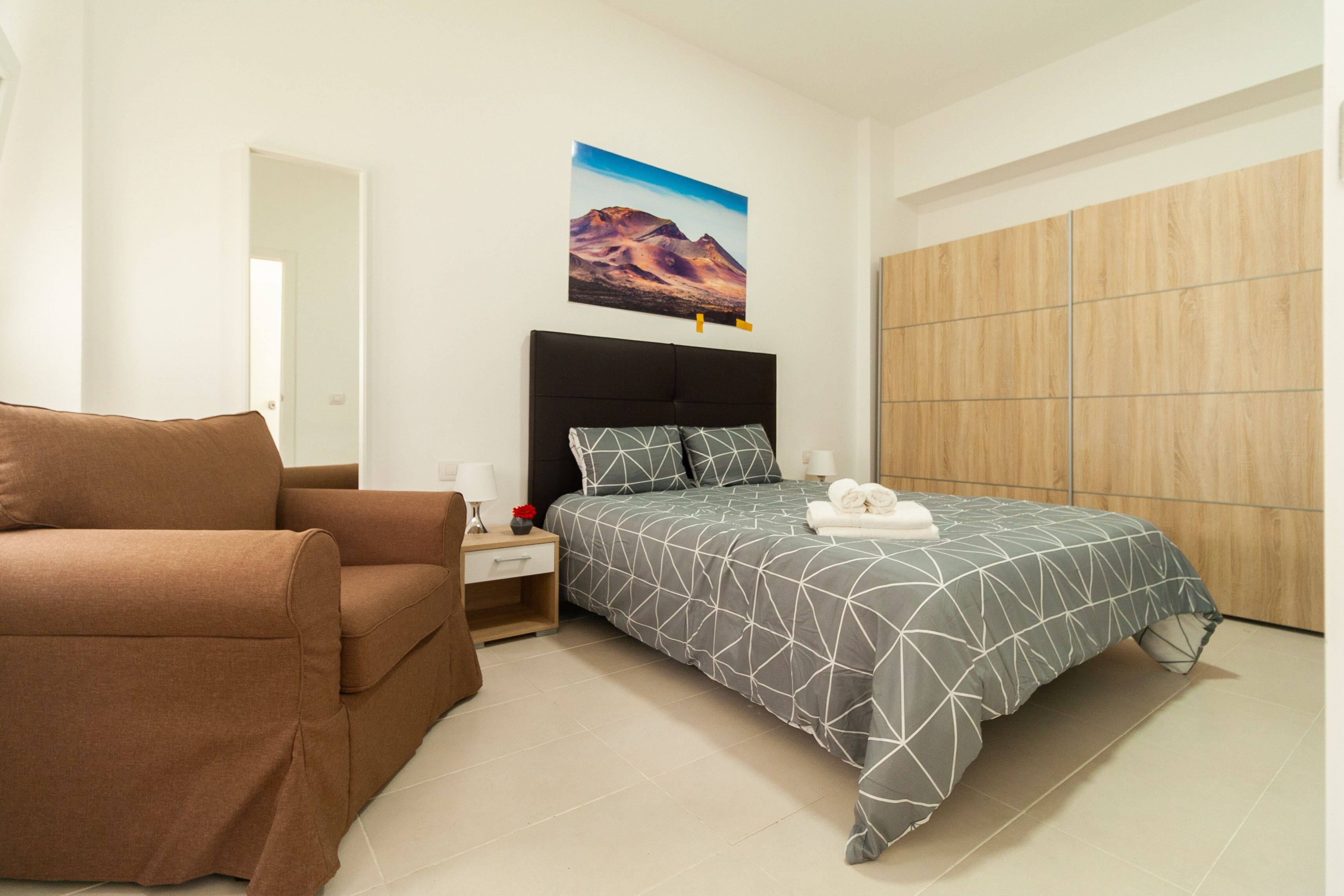Ein Schlafzimmer mit einem Bett, einem braunen Sofa, einem Nachttisch, einem Wandbild und einem Holzschrank.