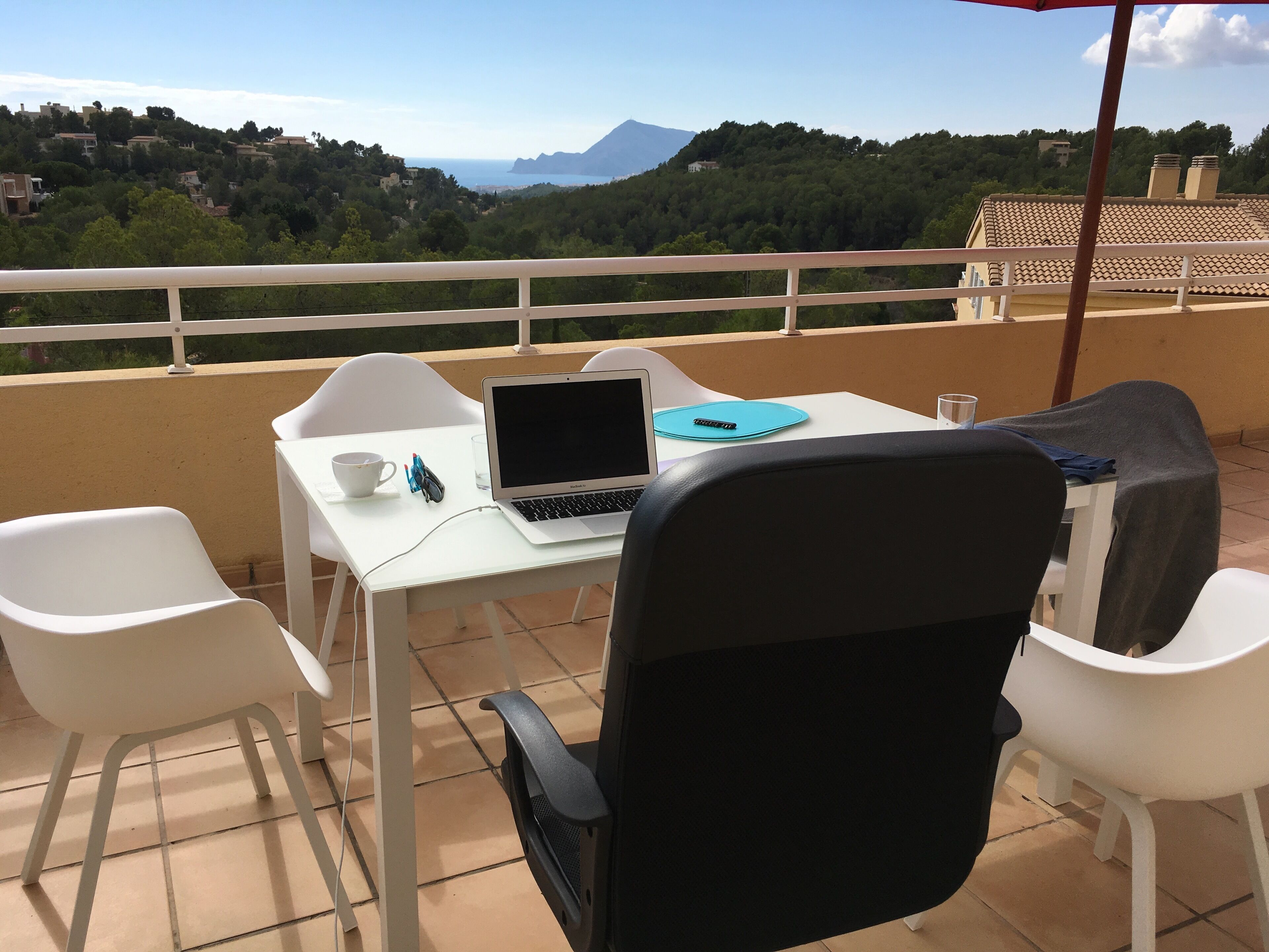 A balcony with a white table, a laptop, a cup, and a glass.
