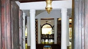 A corridor with white columns, a patterned ceiling, and a chandelier.