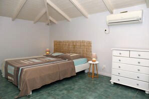 Un dormitorio con cama, mesitas de noche, cómoda, aire acondicionado y cabecera de bambú.