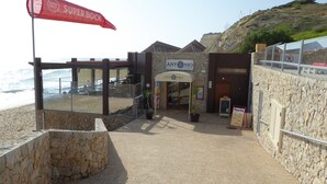 En kystrestaurant med en stenfacade, et rødt Super Bock banner og udsigt over havet.