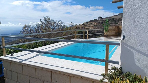 A rectangular pool with a clear blue water surface, surrounded by a white tiled deck and a metal railing.