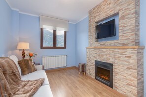 Ein Wohnzimmer mit Kamin aus Stein, einem Wand-Fernseher, einer Couch mit Felldecke und einem Fenster mit Bergblick.
