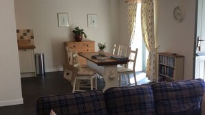 A living room with a sofa, a dining table with chairs, a kitchen area, and a bookshelf.