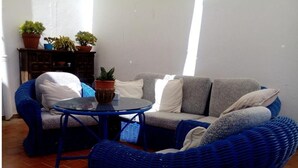Zona d'estar amb un sofà de vimet blau, una taula rodona i plantes en testos.