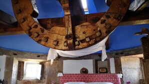 Une chambre rustique avec des poutres apparentes, un lit recouvert de draps blancs, une tête de lit rouge à motifs et un mur en pierre.