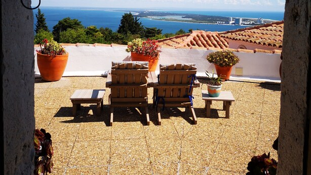 Une terrasse avec des sièges extérieurs, des plantes en pot et une vue sur la mer et les bâtiments.