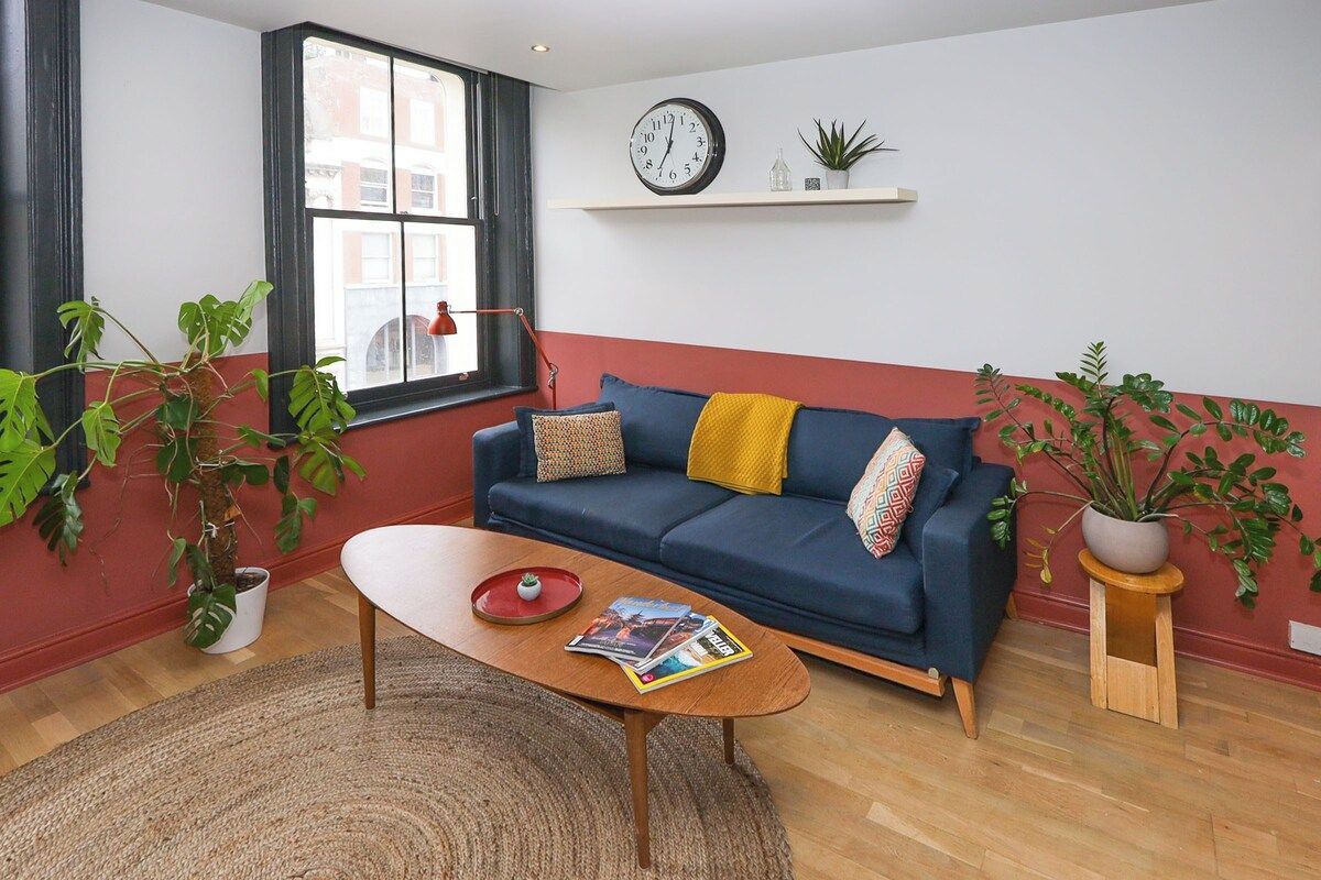 A living room with a blue sofa, a wooden coffee table, a red rug, and potted plants.