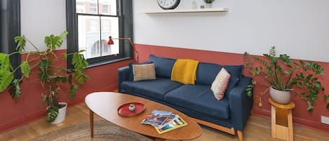 A living room with a blue sofa, a wooden coffee table, a red rug, and potted plants.