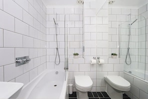 Un baño moderno con bañera, dos inodoros y zona de ducha.