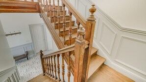 A wooden staircase with a handrail, white walls, and a patterned floor.