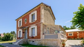 A two-story brick house with a balcony, a stone staircase, and a gravel driveway.