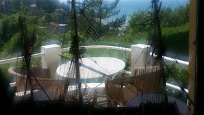 A balcony with wicker furniture, a round table, and a view of the sea and distant hills. - BLUE ROOM FOR RENT TWO STEPS FROM THE SEA (Ault)