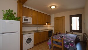 Uma cozinha compacta com armários de madeira, máquina de lavar, micro-ondas e um espaço de jantar com mesa e cadeiras.