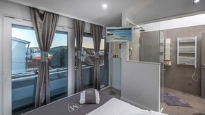 Ein modernes Hotelzimmer mit Bett, Dusche, Blick auf die Stadt und einem großen Fenster mit Vorhängen.