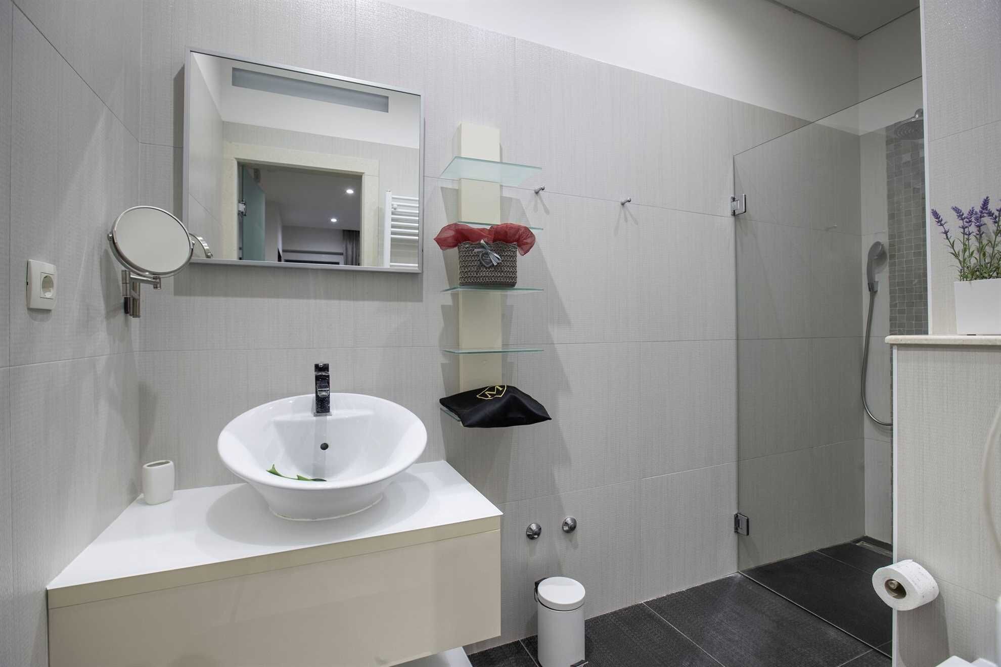 Une salle de bain moderne avec un lavabo blanc, un miroir et des étagères en verre.