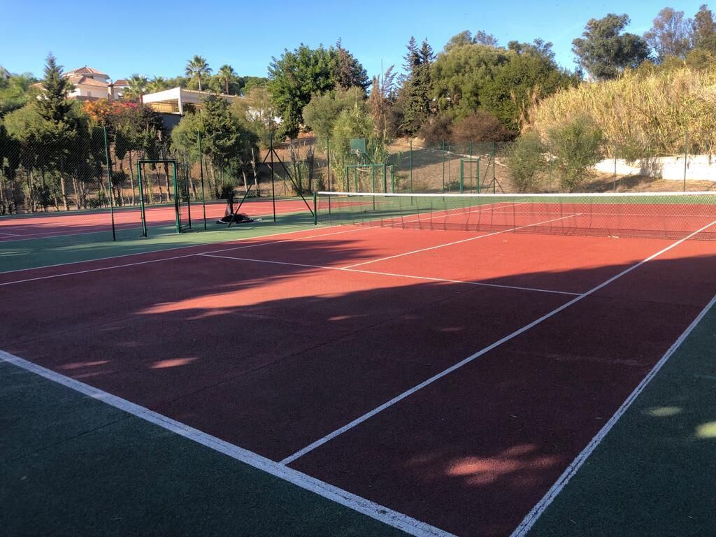 A tennis court with a green and red surface, surrounded by trees and a fence.