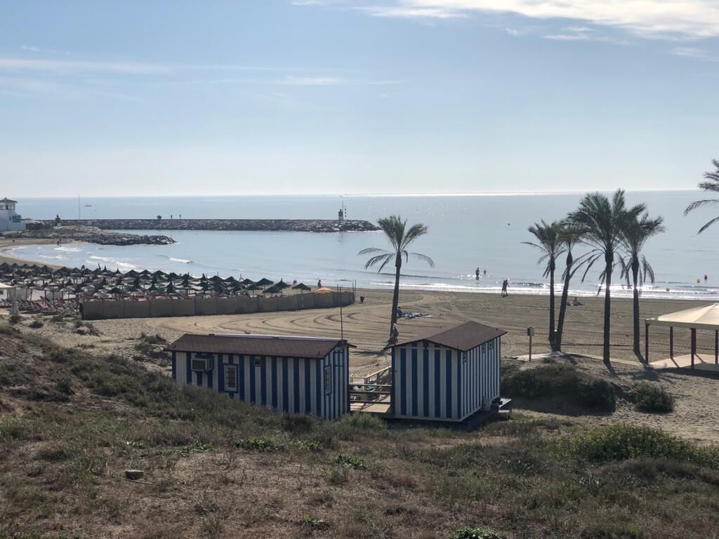 Une vue sur la côte, avec des cabanes de plage, des palmiers et une jetée en arrière-plan.