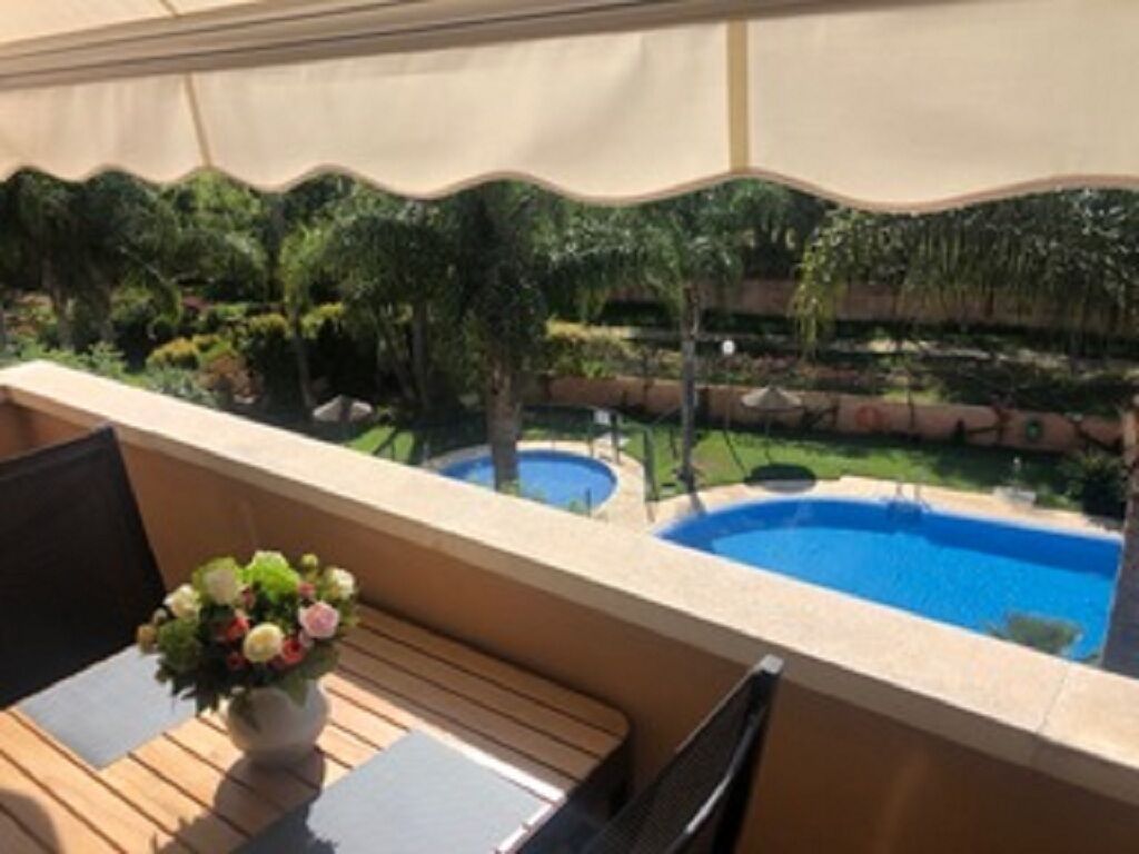 Un balcon donnant sur une piscine, un petit jardin et une table avec des chaises.
