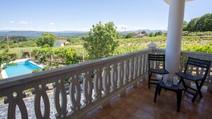 Een balkon met uitzicht op een wijngaard, een zwembad en een tafel met stoelen.