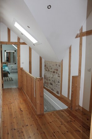A wooden staircase leading to a bedroom with a stone wall and a skylight.