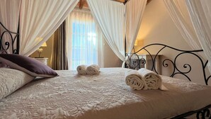 A neatly made bed with rolled towels, a purple pillow, and a canopy bed frame.