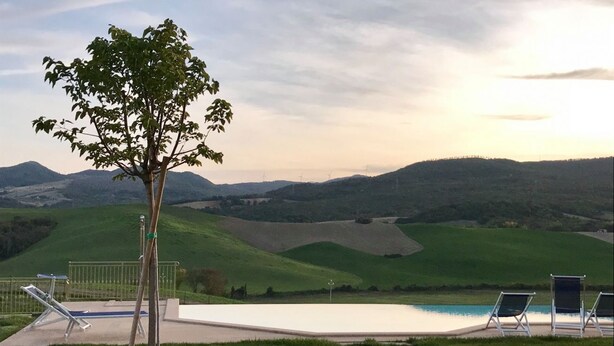 A poolside area with lounge chairs and a tree, overlooking a valley with hills and wind turbines.