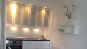 A compact kitchen with white cabinets, a built-in oven, and a sink. There's a small dining table with a chair, and a sofa with a cushion.