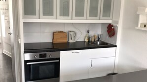 A modern kitchen with white cabinetry, a black countertop, and a dining table with a white chair.