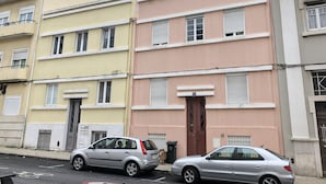 A row of three-story residential buildings with balconies, a bicycle parked in front, and a car parked on the street.